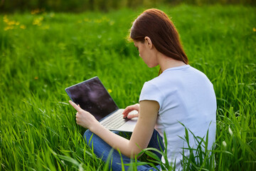 a woman sits at work in a laptop being outdoors in a field