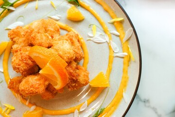 Delicious fried chicken with citrus orange sauce and flower petals decoration in a dish top view on the marble table