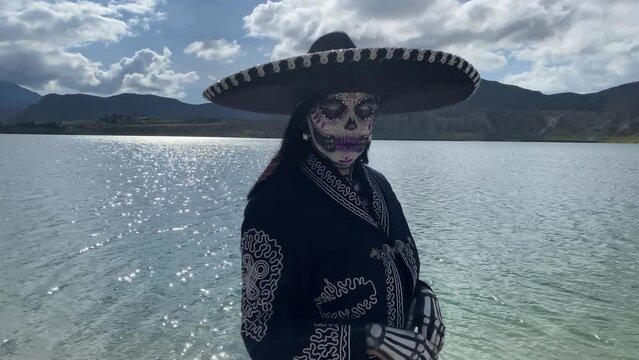 Person in shore of lake disguised as Mexican dead of the day catrina skull looking at camera.