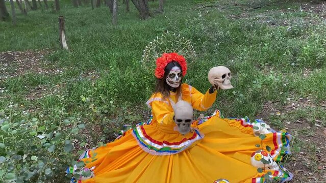 Woman in the woods disguised as a Mexican catrina sitting holding human skulls in her hand. Ritual in Day of the Deads. 