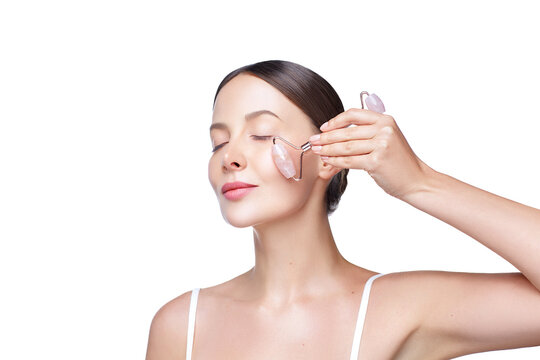 Portrait of young woman using jade roller for self facial massage isolated on white background. Beauty procedure. Skin therapy. Dermatology. Skincare routine