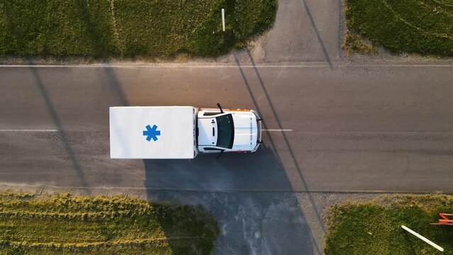 Aerial top-down shot of Ambulance driving across screen slowly on road with emergency lights on