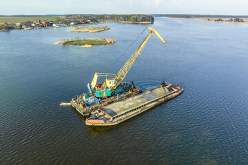 aerial view on crane extracts minerals from bottom onto huge barge in middle of lake or sea