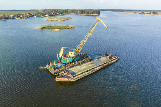 aerial view on crane extracts minerals from bottom onto huge barge in middle of lake or sea