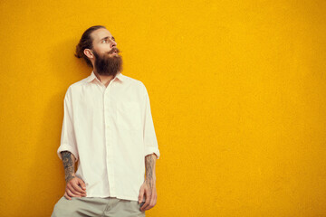 Bearded and tattooed man posing on yellow wall outside. Fashion and style