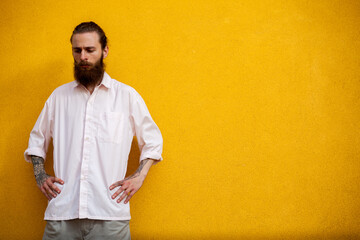 Portrait of tattooed bearded hipster on yellow wall posing outdoor