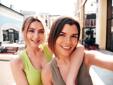 Two young beautiful smiling hipster female in trendy summer t-shirt and shorts clothes. Sexy carefree women posing on street background. Positive models having fun, hugging. Taking selfie photos