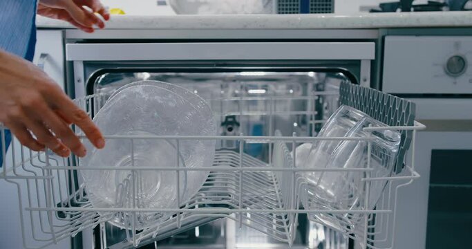 Young woman loading dirty dishes into dishwasher machine. Close-up, top view
