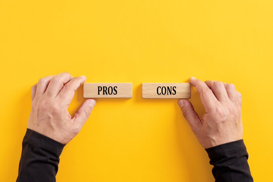 Comparing the pros and cons options. Hands holding wooden blocks with the words pros and cons.