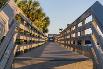 Wooden straight pathway with railings in Destin, Florida. Footbridge near palm trees on the left and parked vehicles on the right.