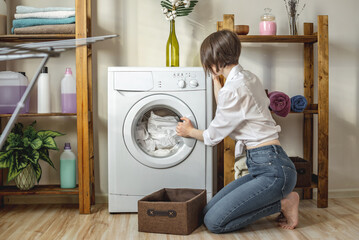 Woman is washing white clothes in a washing machine in a laundry room. The concept of caring for...