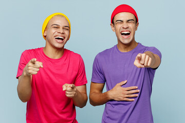 Young cheerful fun couple two friends men wearing casual clothes looking camera together pointing index fingers camera on you laugh isolated on pastel plain light blue cyan background studio portrait.
