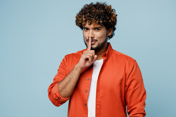 Young secret Indian man wear orange red shirt white t-shirt say hush be quiet with finger on lips...