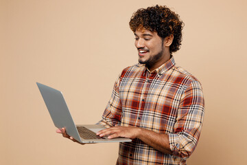 Side view smiling fun young Indian IT man wear brown shirt casual clothes hold use work on laptop...