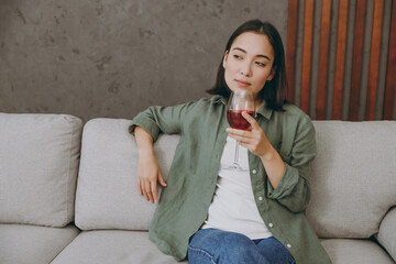 Young calm woman of Asian ethnicity wear casual clothes drink red wine look aside in minded mood...