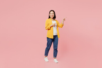 Full body young woman of Asian ethnicity wear yellow shirt white t-shirt point index finger aside indicate on workspace area copy space mock up isolated on plain pastel light pink background studio.