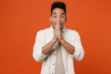 Young surprised shocked happy man of African American ethnicity wear light shirt casual clothes cover mouth with hands look camera isolated on orange red background studio portrait. Lifestyle concept.