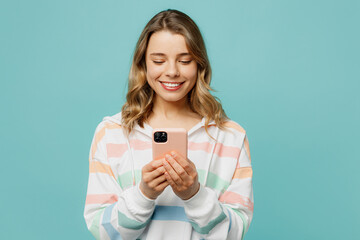 Young smiling cheerful cool blonde woman wear striped hoody hold in hand use mobile cell phone...