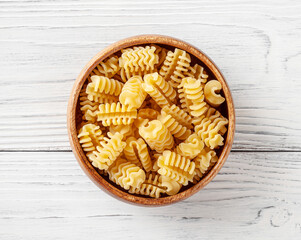 Uncooked radiatori pasta in wooden bowl on white wooden background