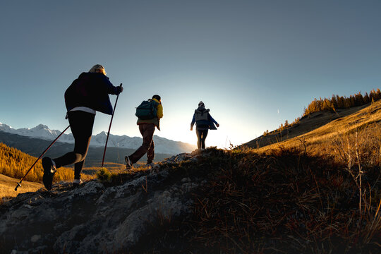 Three active female hikers walks in mountains. Silhouettes of tourists with backpacks at sunset time