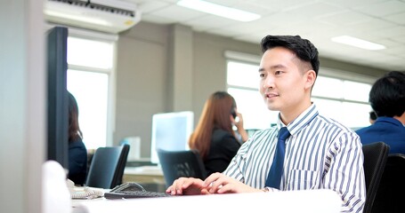 Happy asian young businessman worker typing in a laptop on desk at modern office
