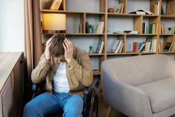 Obraz premium A young handsome man in a wheelchair looks out the window with a sad look