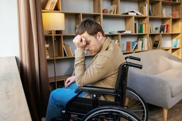 A young handsome man in a wheelchair looks out the window with a sad look