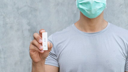 Man holding antigen test kit on a gray background.