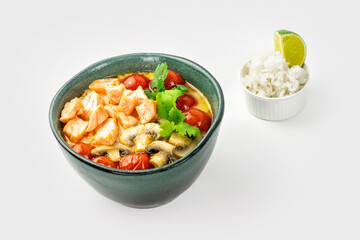 Spicy creamy soup with tofu, cherry tomato, cilantro leaves, mushrooms and little bowl of rice with slice of lime on light background. Asian Thai food