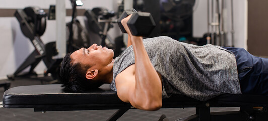 Asian young muscular male fit strong body sporty athletic fitness model in sportswear laying down bench lifting metal dumbbells chest and shoulder training in Crossfit gym with smoke background © Bangkok Click Studio