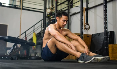 Foto op Canvas Asian young muscular fit strong body sporty athleticshirtless male fitness model sitting on floor taking break after workout exercising weight training in Crossfit gym full gymnastic sport equipment © Bangkok Click Studio