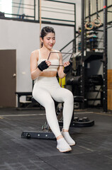 Naklejka na ściany i meble Asian young muscular fit strong body sporty athletic sexy female fitness model sitting smiling taking break holding looking at tablet computer mockup after workout exercising weight training in gym