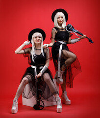 Violinist women duet in the stage costumes on the red background.