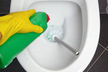 Person in yellow rubber gloves cleans the toilet bowl with a brush and disinfectant