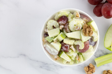 Bowl of waldorf salad with apple, celery, grapes, walnuts and yogurt on a white background. Top view. Copy space.