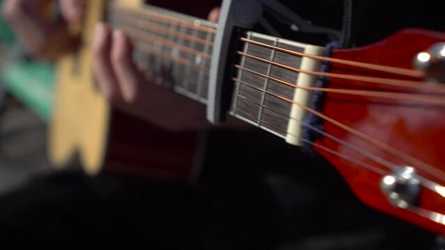A young man plays the acoustic guitar. A man plays the guitar close-up. The camera will move away.