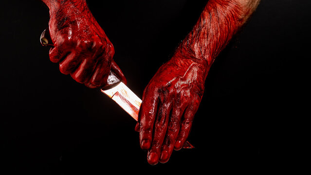 A man wipes a bloody knife with his hand on a black background. 