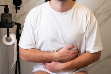 Man in a white T-shirt with abdominal pain is sitting on the toilet. 
