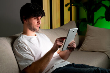 A man is sitting on the sofa and using a computer tablet to browse the Internet or online shopping via unlimited wireless Internet. 