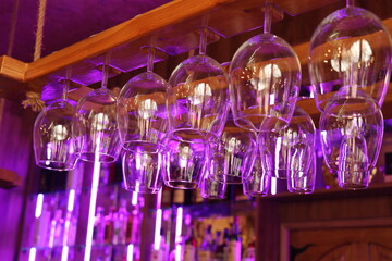 Wine glasses hang over the bar counter with purple lighting