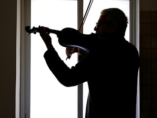 Silhouette of a violinist on the background of the window.