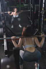 Fototapeta premium A young and fit woman does barbell squats at the gym. Using the bar weight only.