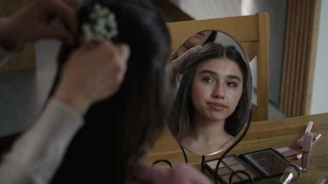 Mirror reflection of caucasian woman doing hairstyle for her daughter for prom. Shot with RED helium camera in 8K.   