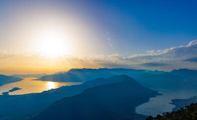 Fototapeta na wymiar Dazzling sun in the evening sky illuminates all the peaks of the Balkan Montenegrin mountains and the coast of Kotor Bay
