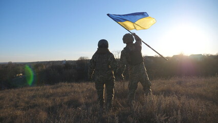 Dolly shot of young woman and man in military uniform waving flag of Ukraine against sunset. Female...