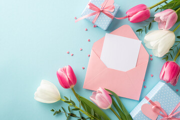 Mother's Day concept. Top view photo of open envelope with letter present boxes with bows pink white tulips and heart shaped sprinkles on isolated pastel blue background with blank space