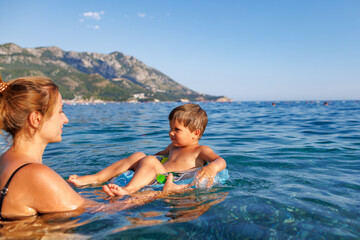 Caring mother rides her son on an inflatable ring in the sea