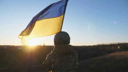 Female ukrainian army soldier lifting national banner in hill. Young woman in military uniform...