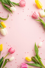 Fototapeta na wymiar 8-march decorations concept. Top view vertical photo of yellow pink white tulips and sprinkles on isolated pastel pink background with empty space in the middle