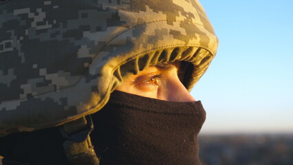 Gaze of male ukrainian army soldier in helmet and balaclava outdoor. Profile view of young military man looking with hope at sunset. Invasion resistance. War between Russia and Ukraine. Close up